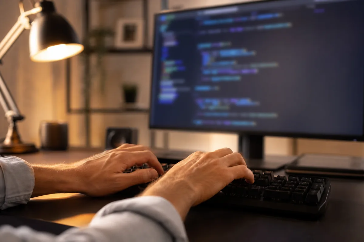 Mains sur un clavier devant un écran affichant un éditeur de code flouté, ambiance de bureau français